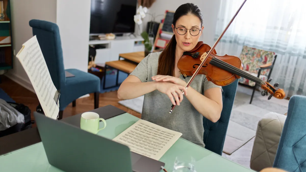 An adult, dressed in a colorful long sleeve and eyeglasses, sits attentively at a sleek digital keyboard, their fingers moving gracefully over the keys. The soft glow of a tilt light bathes the scene, casting an inviting, warm ambiance around them.