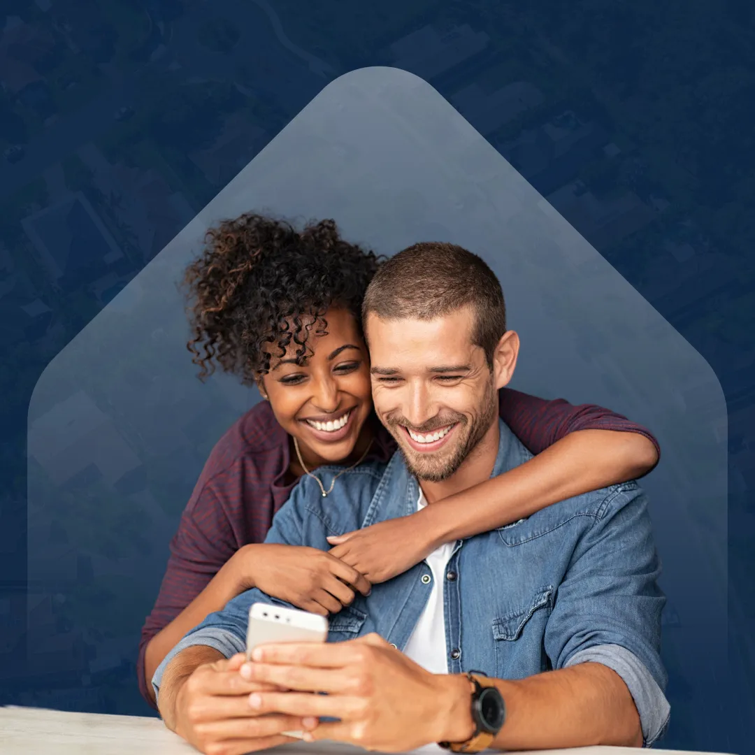 Smiling couple looking at a smartphone together, with the woman hugging the man from behind, set against a subtle house-shaped background overlay.