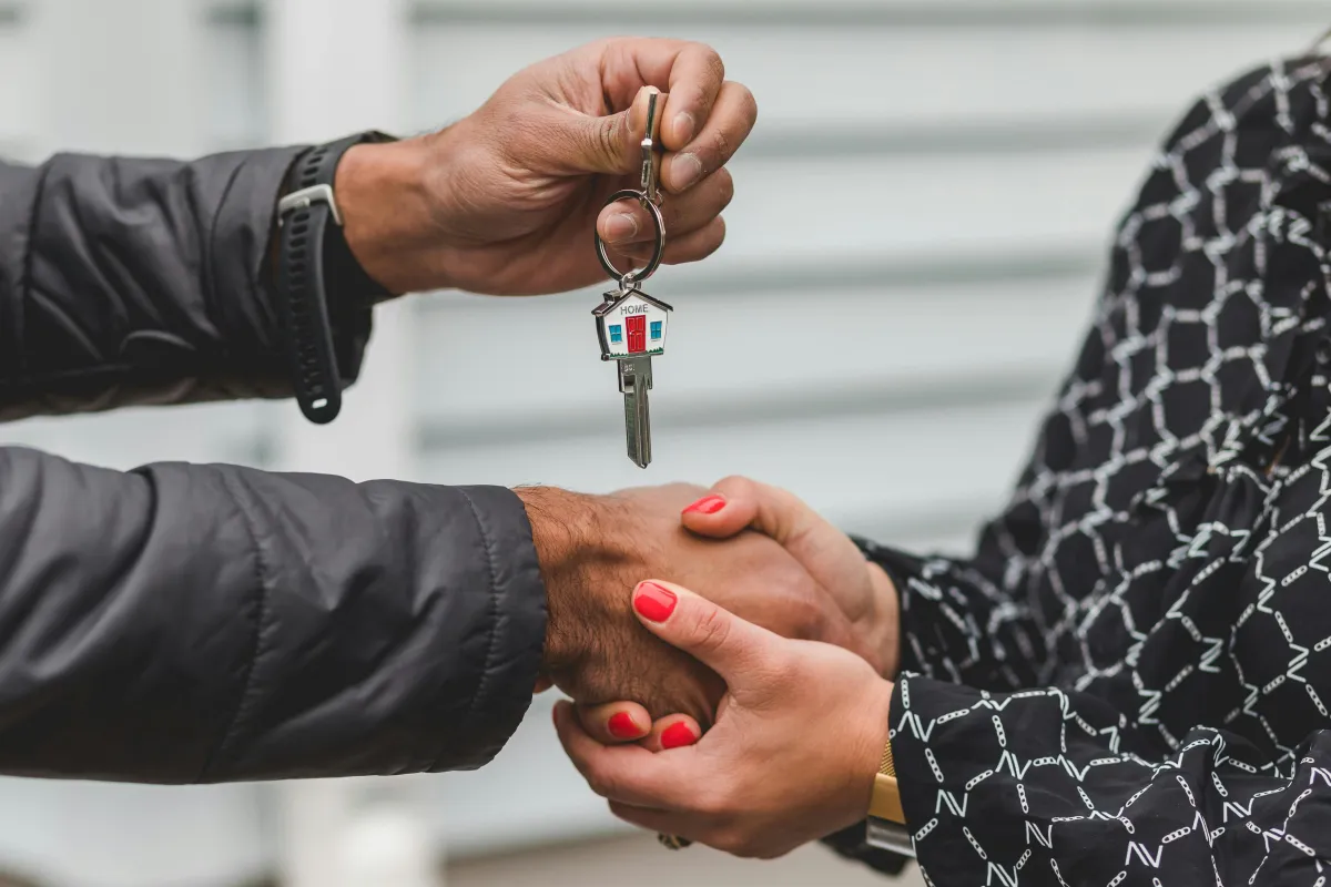 A close-up of two people exchanging house keys, symbolizing the completion of a home purchase or lease agreement.