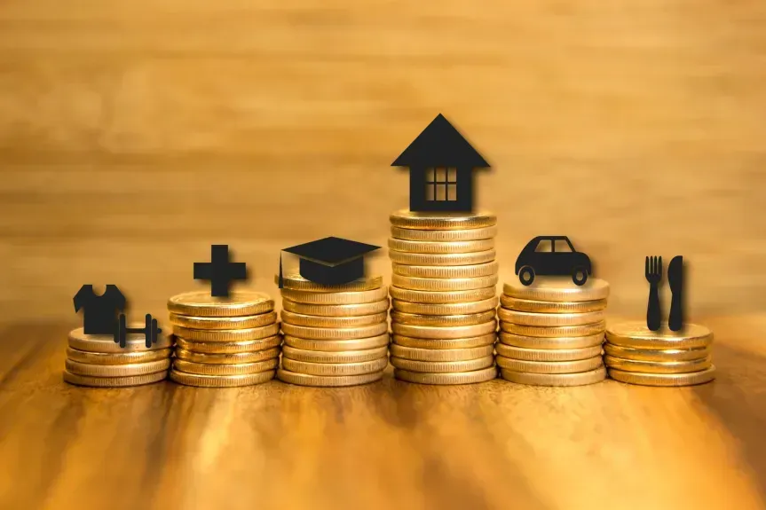 Stacks of coins arranged at different heights, each topped with icons representing expenses like clothing, healthcare, education, housing, transportation, and dining.