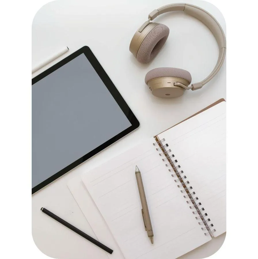 Image of an iPad, headphones and notebook and pen on a desk
