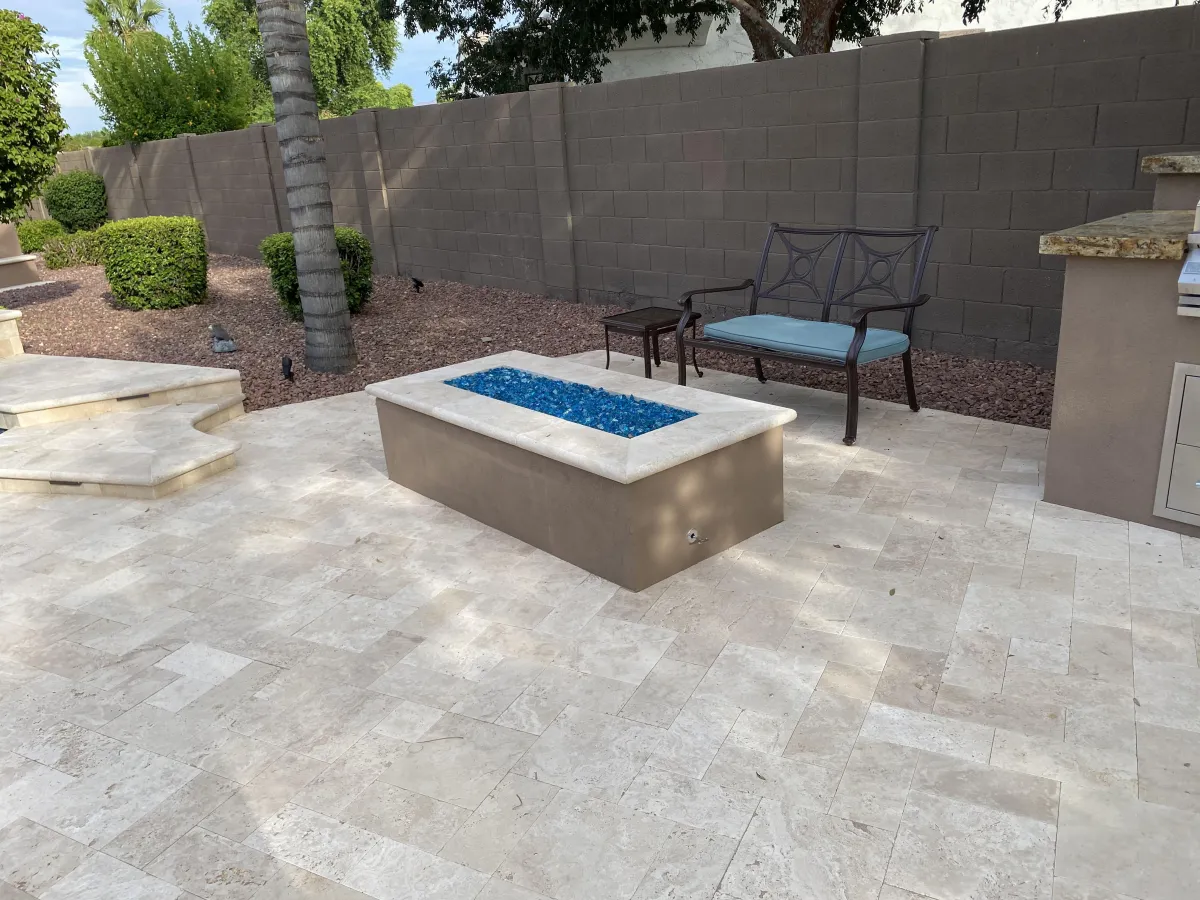 Custom-designed fire pit with a sleek modern finish on a travertine patio, creating a cozy outdoor seating area.