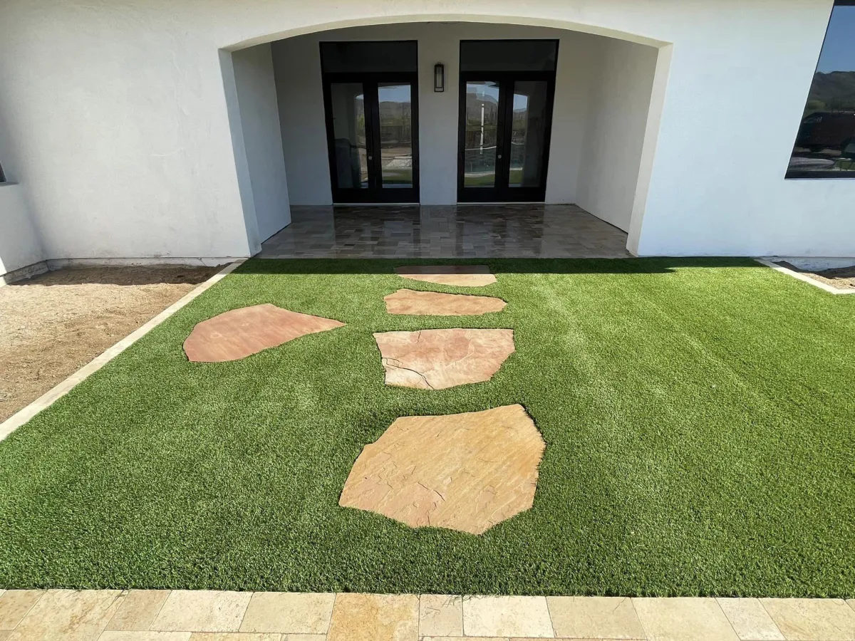 Front yard landscaping with artificial grass and custom stone pathway leading to a modern home entrance