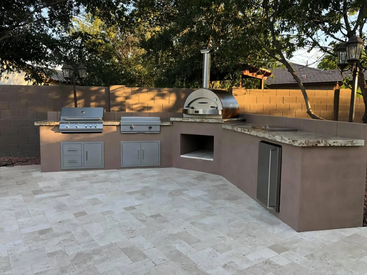 Modern outdoor kitchen with built-in grill, pizza oven, and storage on a custom paver patio