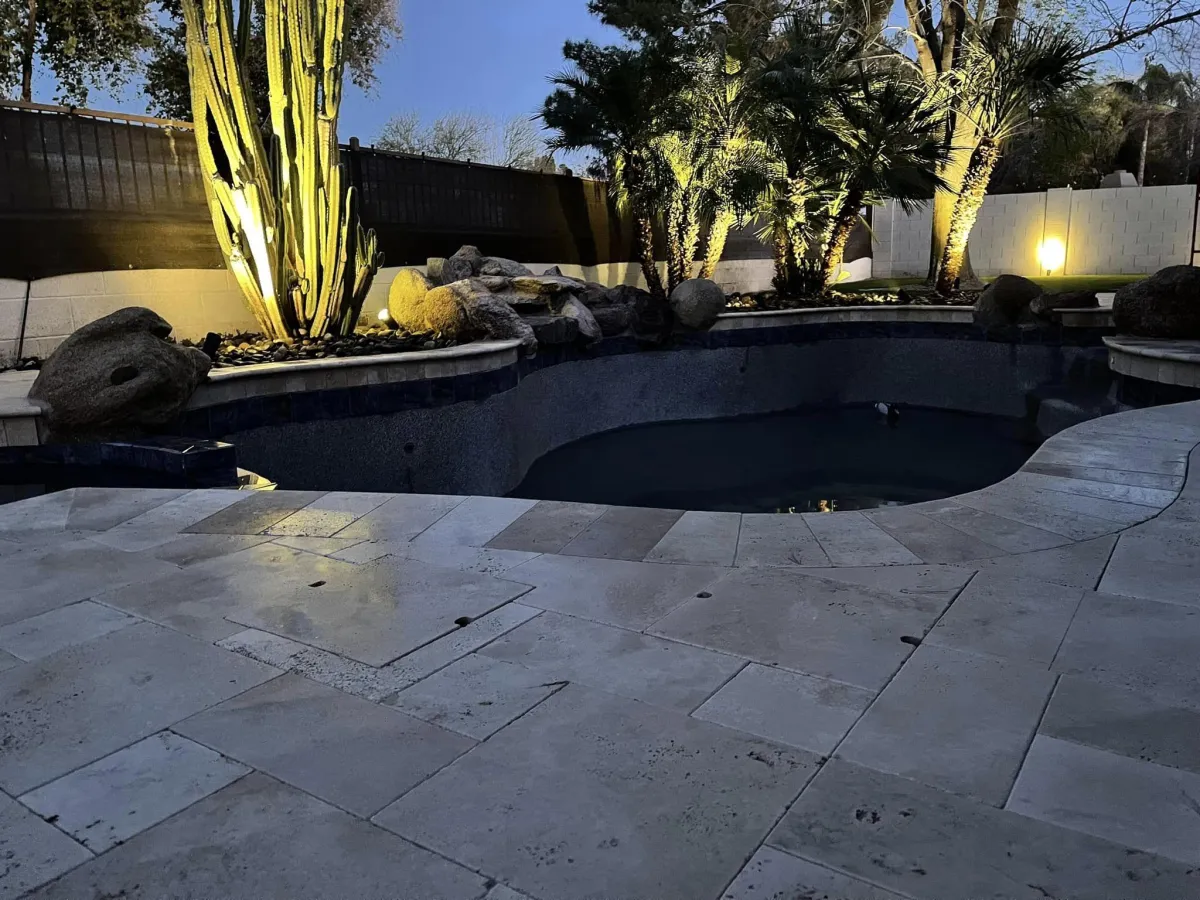 Luxurious backyard pool area with travertine patio and energy-efficient outdoor lighting for ambiance and safety.