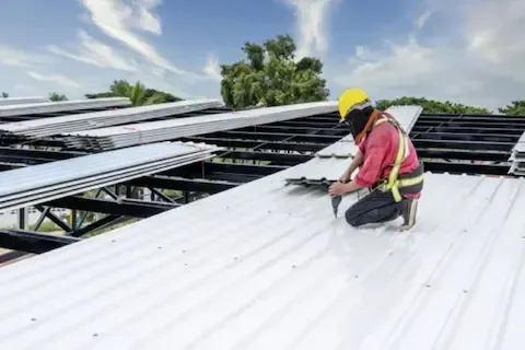 Roofer in safety harness fastening white metal roof panels on a commercial building in Maple Grove