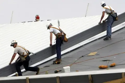 Three workers with fall protection securing metal panels on sloped commercial roof by Maple Grove Commercial Roofing