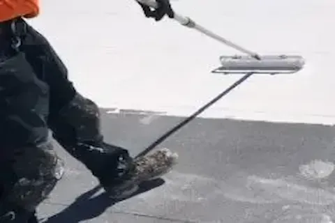 Worker rolling liquid coating across flat commercial rooftop surface