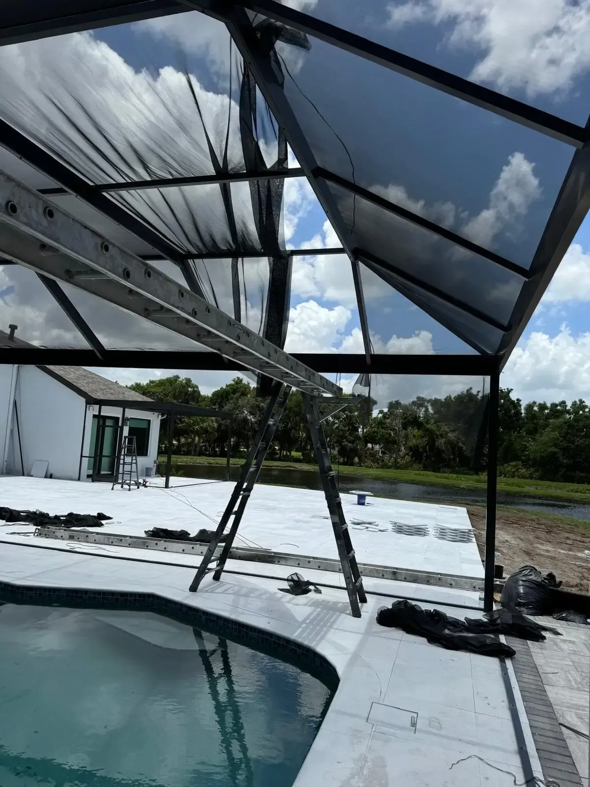 Pool enclosure under repair with a ladder propped against the metal frame and torn screen mesh hanging above the pool