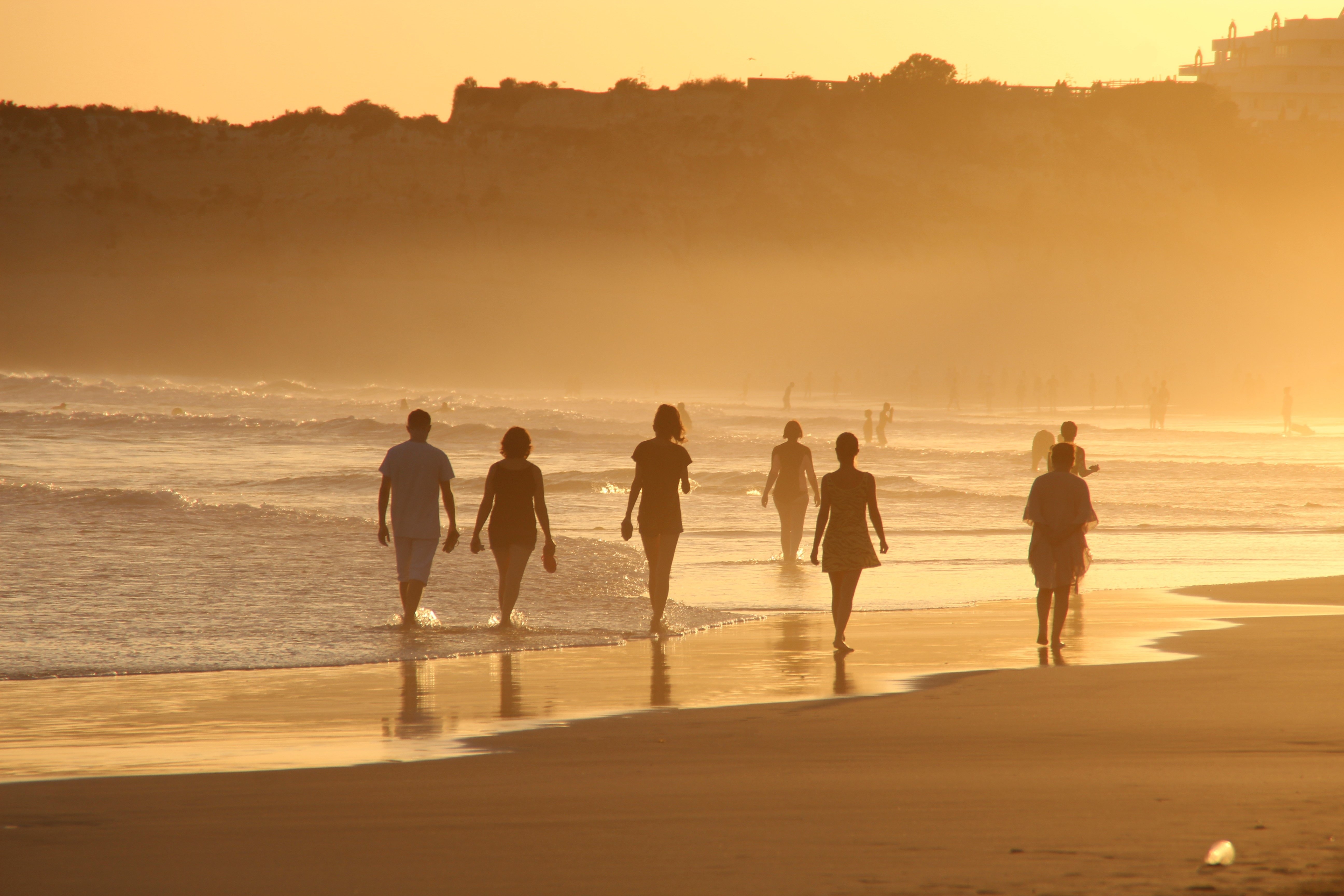 group of people walking along the beach at sunset