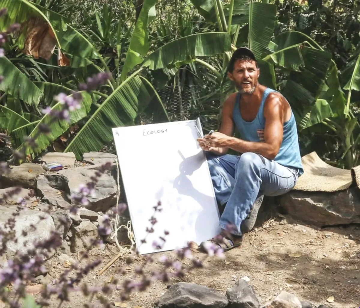 Neal Hegarty is holding a white board teaching students about Guatemala permaculture