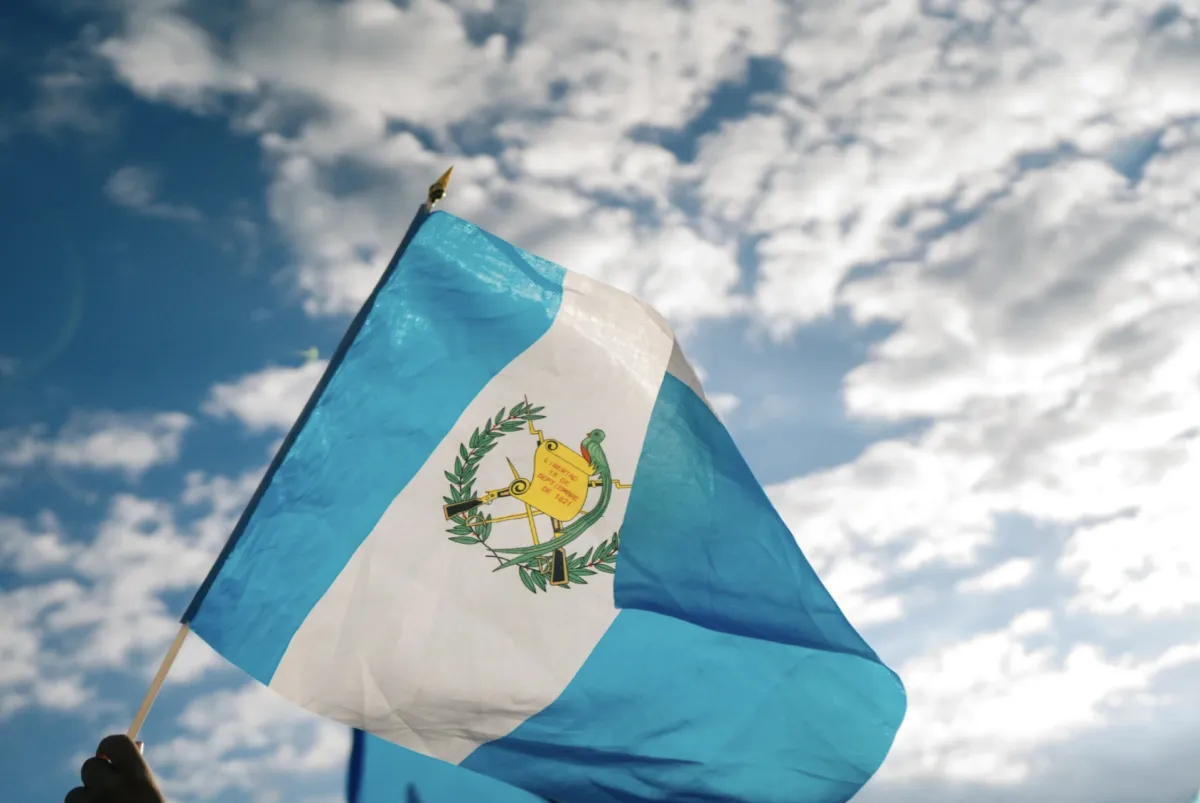 A Guatemalan flag is waved in the air on a sunny day with clouds in the sky