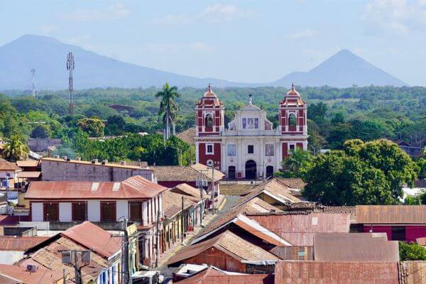 A large red and white church stands above the town with volcanoes in the background of Leon Nicaragua