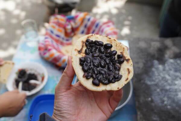 A hand holds a freshly made tortillas filled with black beans, an example of vegan food in Guatemala