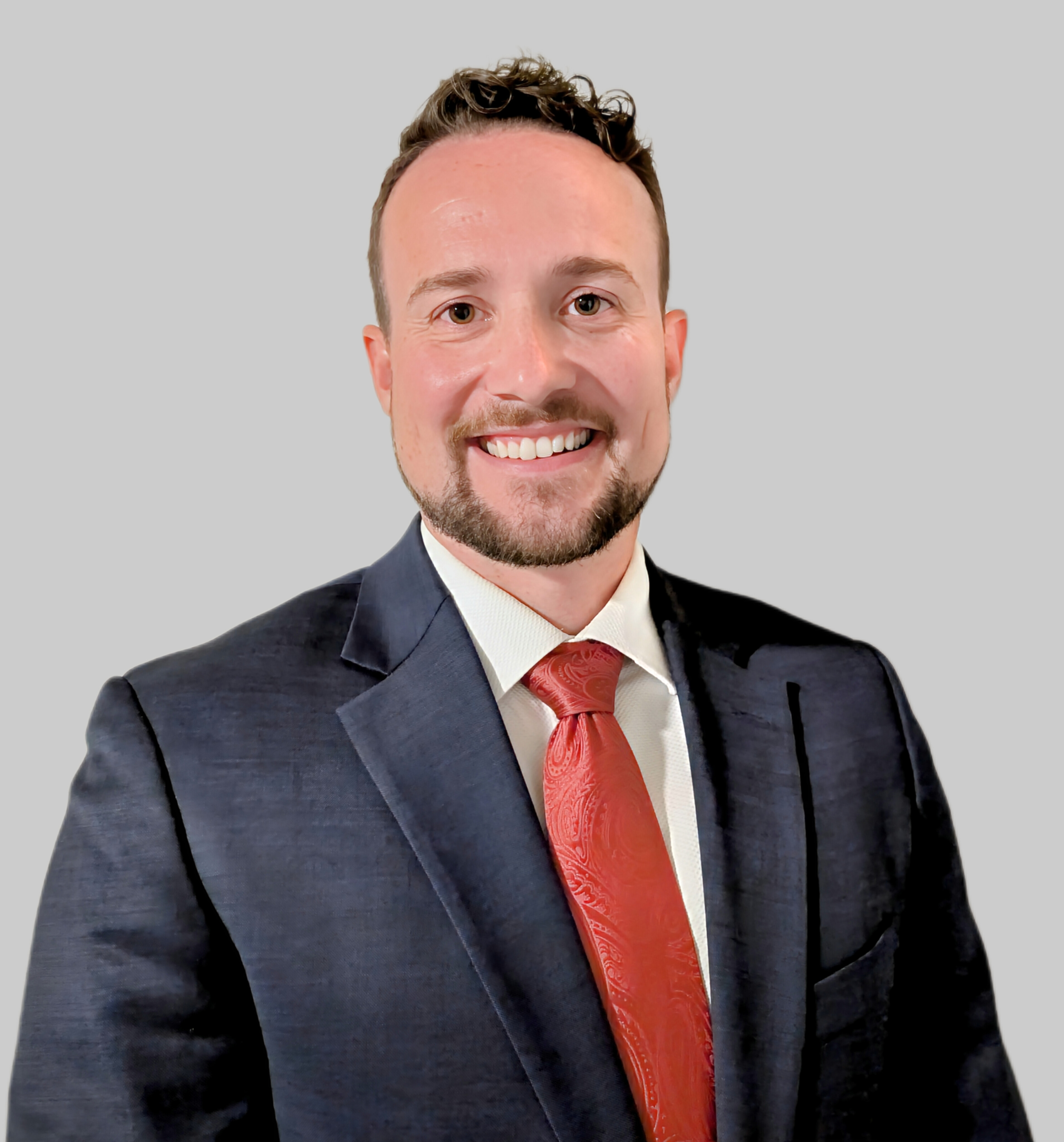 Chadd Johns, an African American man in his late 40s, wearing a tailored gray blazer and blue shirt, standing in front of a bookshelf filled with finance books. He exudes warmth and professionalism, with a welcoming smile.