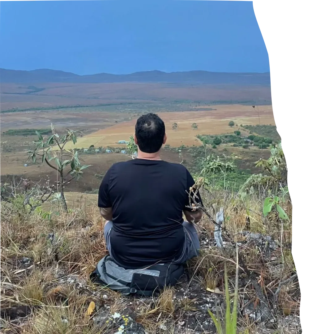 Mulher sorrindo sentada em pedra, meditando em meio à vegetação da Chapada, luz suave do entardecer, expressão serena, roupas leves, cenário natural ao fundo
