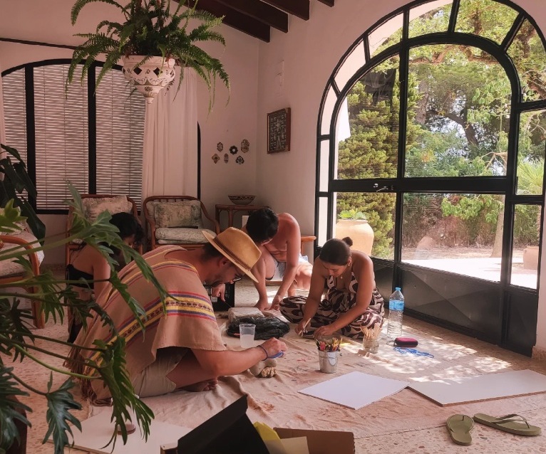 Participants painting together in a cozy, sunlit room with art supplies and soft earth tones