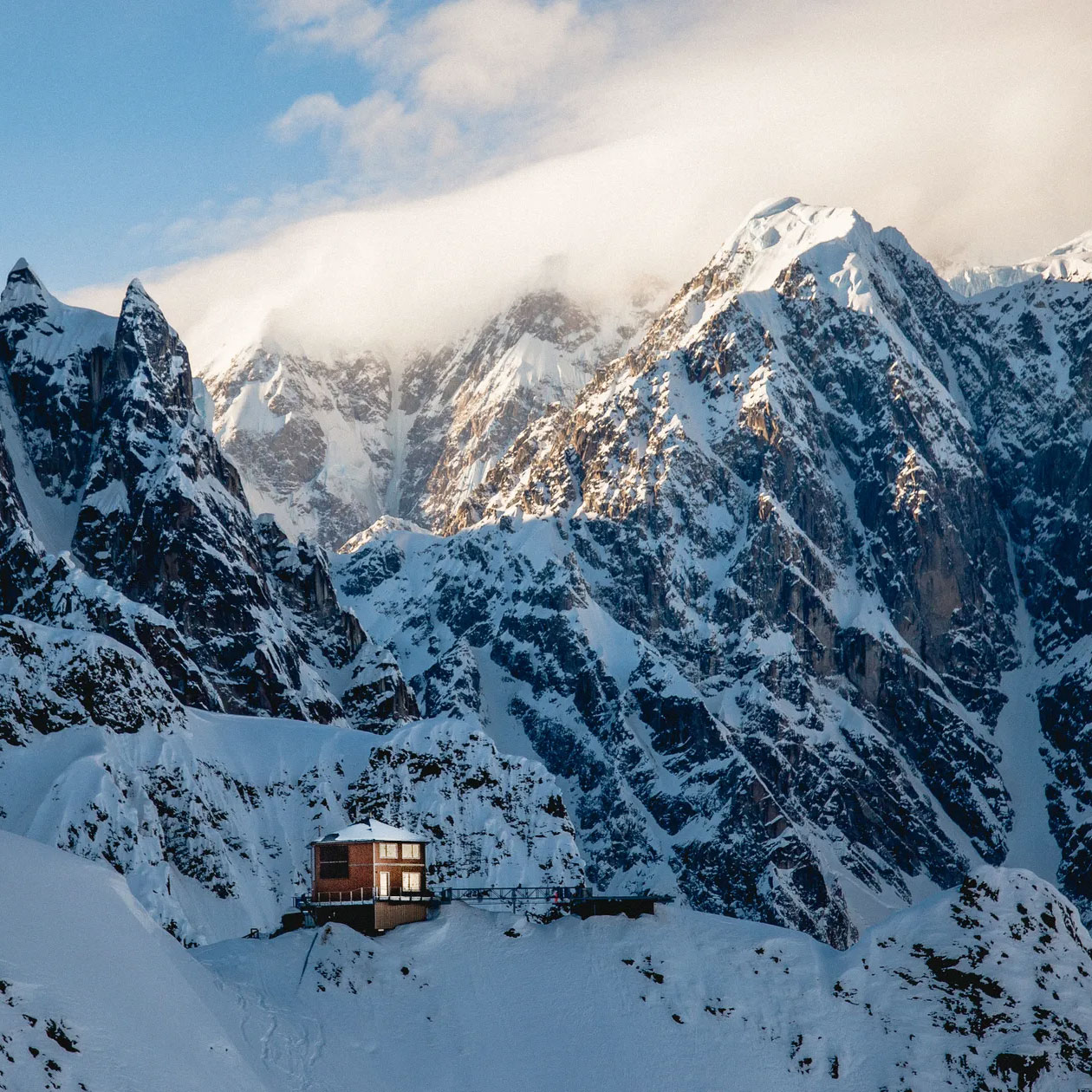 Snow-covered mountains surrounding Sheldon Chalet, an exclusive Alaskan destination, showcasing a modern lodge against a dramatic alpine backdrop.