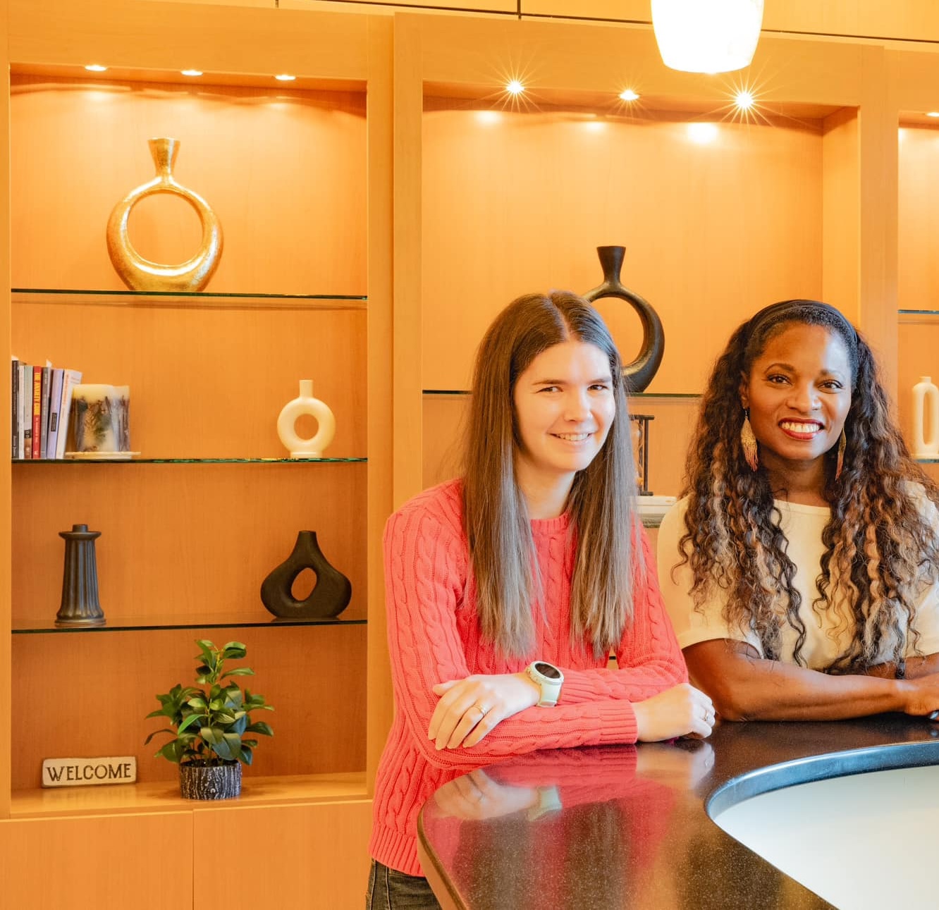 Business owner smiling at a modern reception area, with decorative shelves featuring vases and books, emphasizing a welcoming atmosphere for a therapy practice.