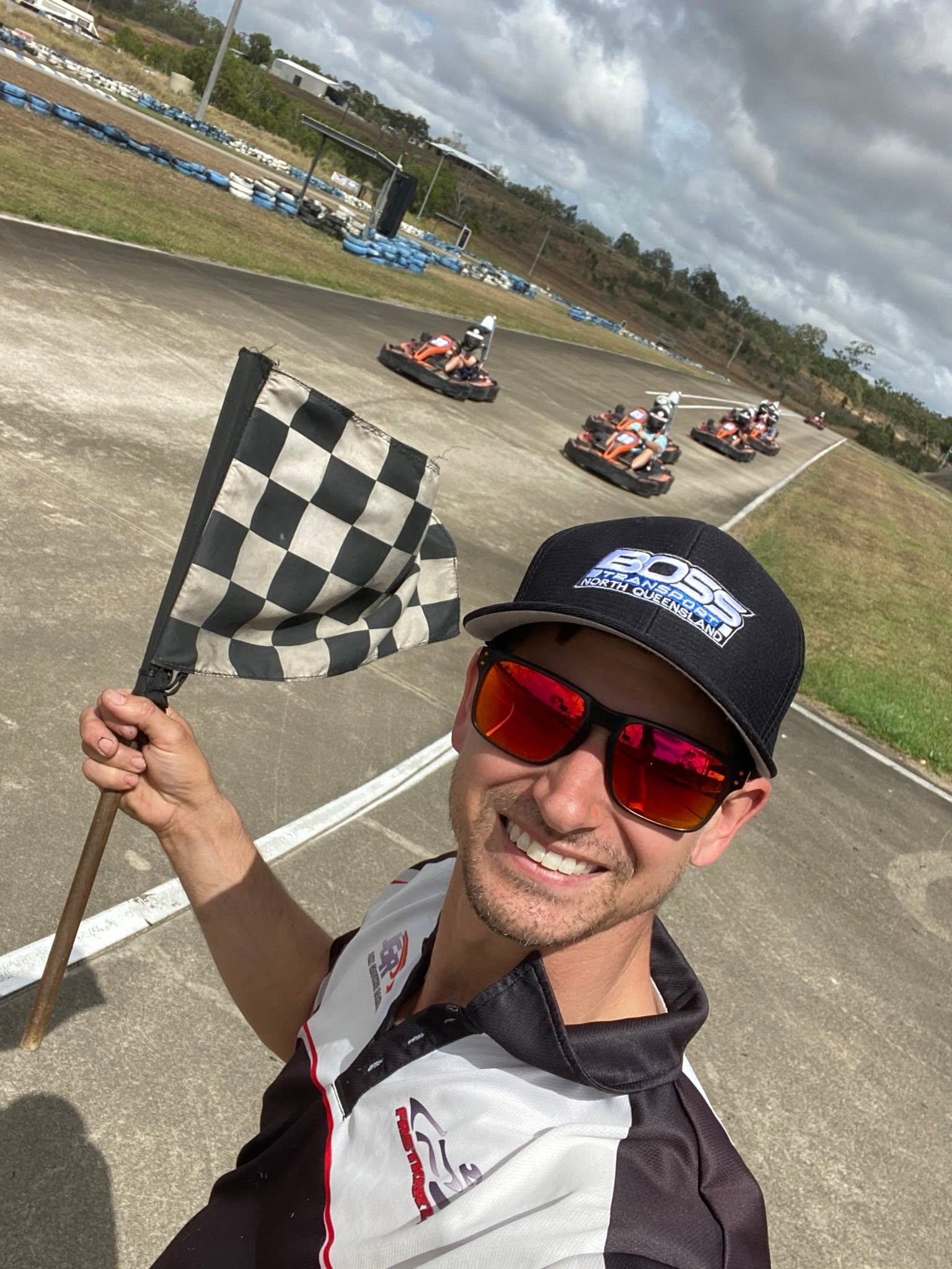 FastKarts team member holding a chequered flag with drivers on the track