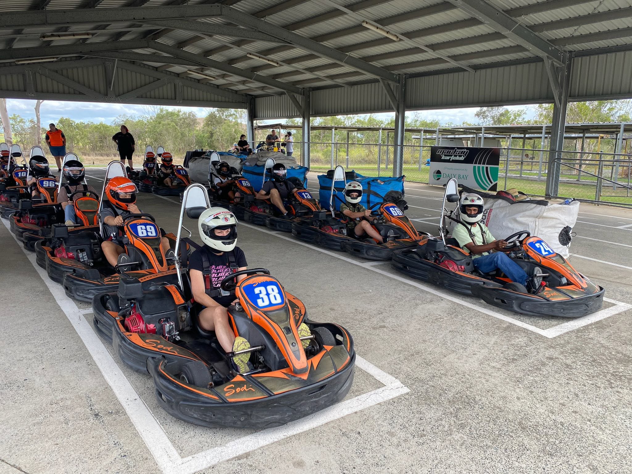 Helmeted FastKarts drivers lined up in orange and black karts, ready to race
