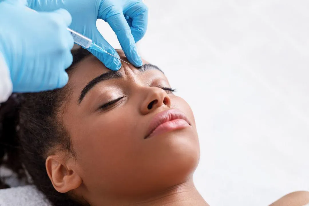A woman receiving a Botox injection in the forehead while lying down, showing a professional treatment in a clinical setting.