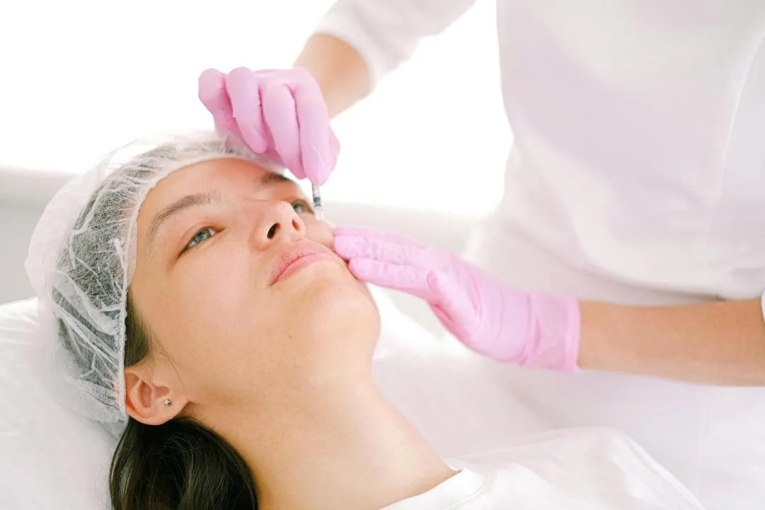 Woman receiving Botox injection on forehead from medical professional wearing pink gloves, focusing on safety, precision, and risk reduction.