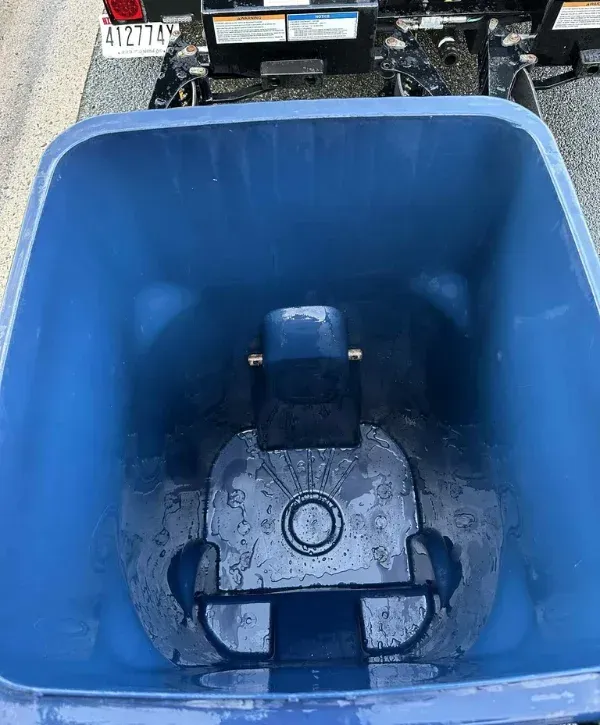 A close-up, top-down view inside a wet, empty blue dumpster with water droplets on the bottom surface.