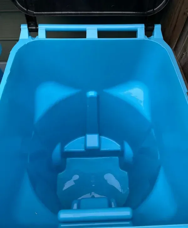 A close-up, top-down view inside a clean, empty blue plastic recycling bin, showing its textured bottom.