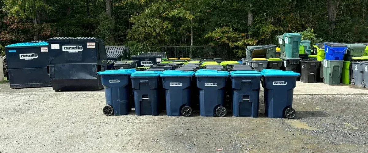 A wide view of a Casella yard filled with various sizes of blue, green, and black recycling bins and dumpsters.