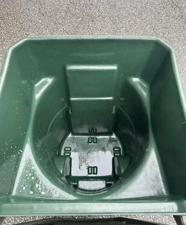 A close-up, top-down view of a dark green plastic spreader hopper with water droplets on its interior.