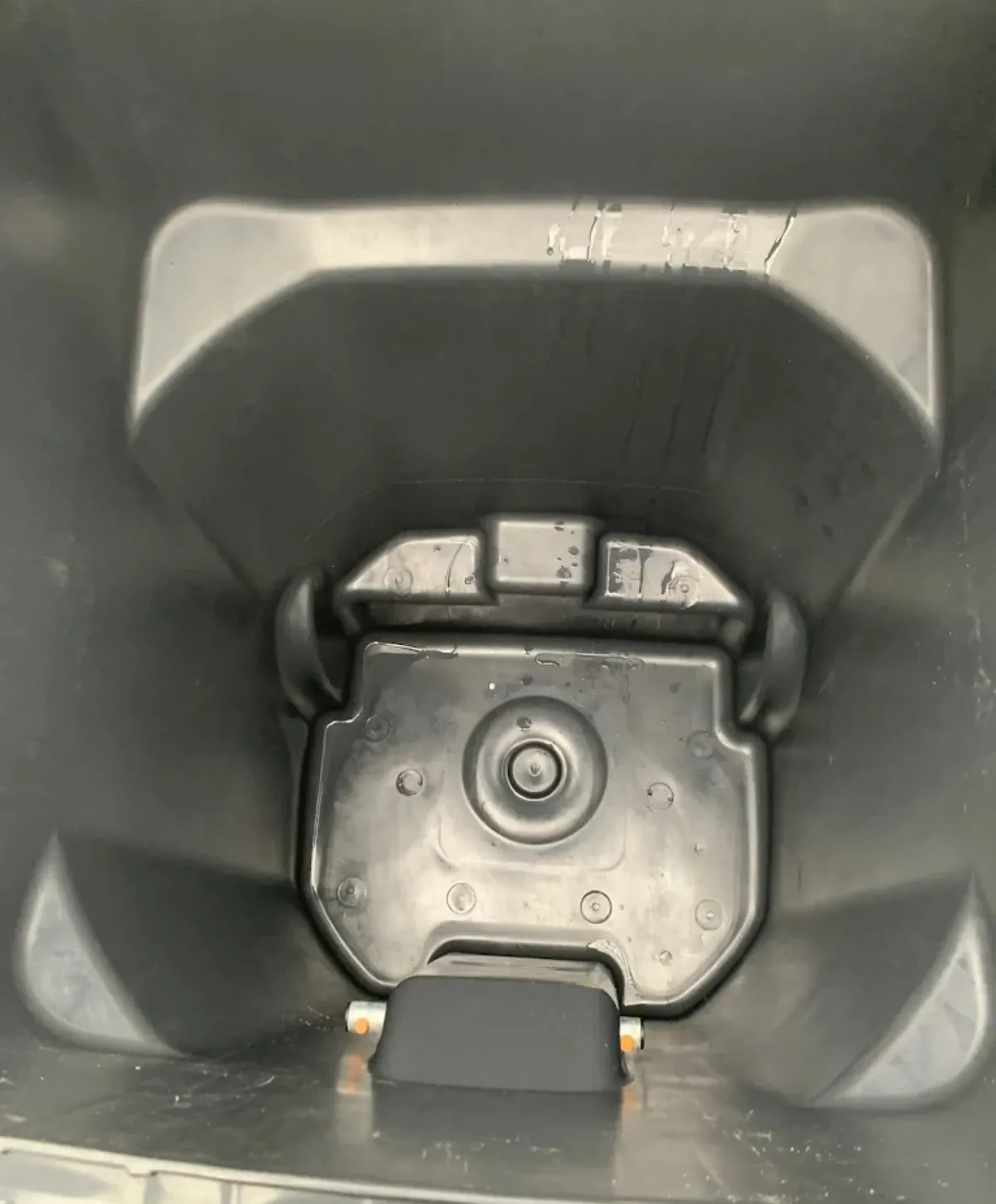 Inside view of a dark gray plastic waste bin, showing the bottom mechanism and worn interior surfaces.