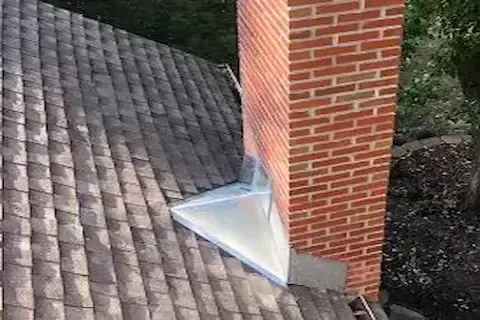 New metal chimney flashing sealed at the base of a brick chimney on shingle roof