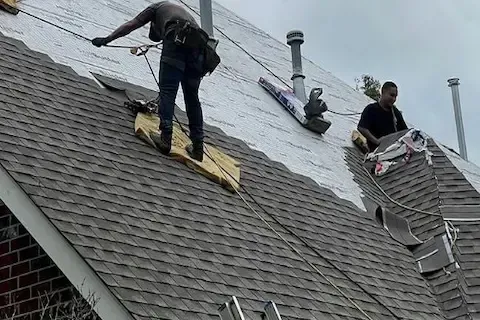 Two roofers removing old shingles on a residential roof replacement by Blaine Roofing