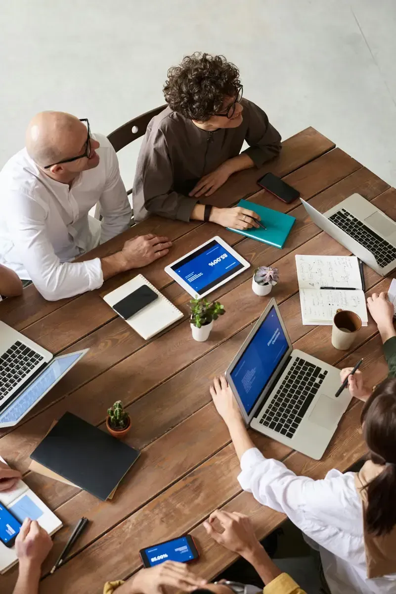 Team sitting around the boardroom table with computers and tablets.