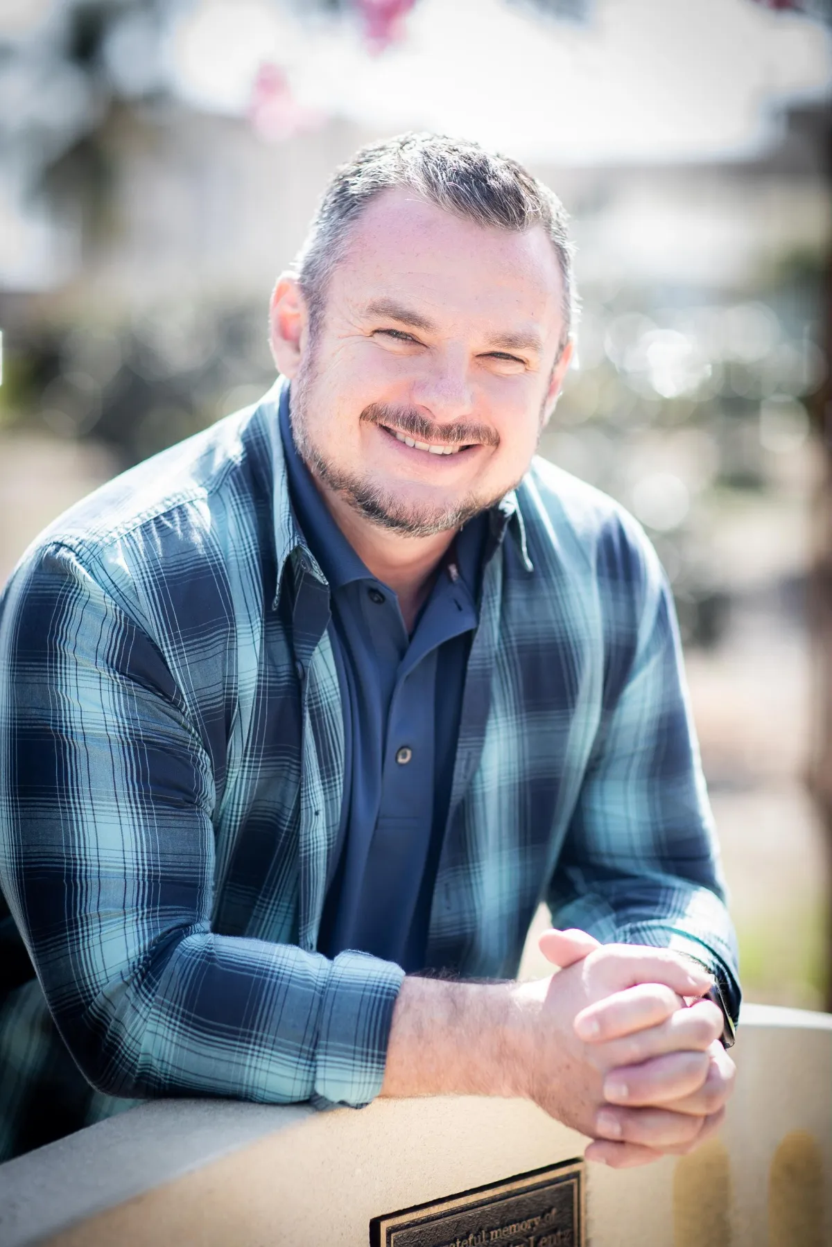 A charismatic middle-aged man with salt-and-pepper hair, wearing a smart blazer and open-collar shirt, smiles confidently in a well-lit studio. The background features bookshelves and a microphone, suggesting expertise in communication and coaching. The portrait is warm and inviting.