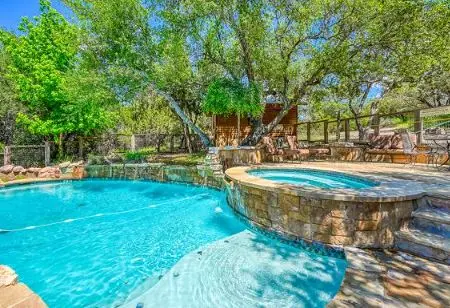 Natural stone pool and raised spa under oak trees receiving pool service from Canyon Lake Pool Service