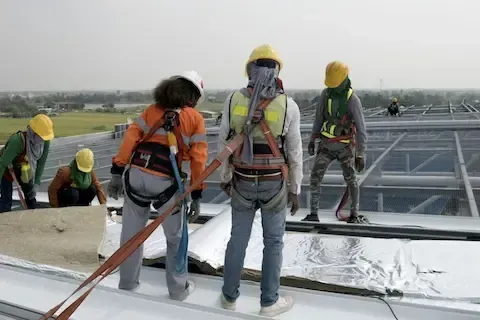 Safety-harnessed crew laying insulation sheets on large commercial rooftop in Plymouth