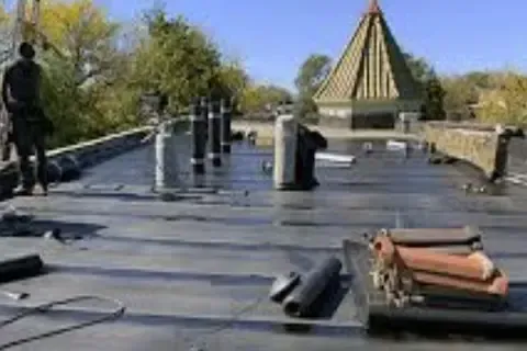 Plymouth Commercial Roofing installer rolling out flat roof membrane with pipe boots visible