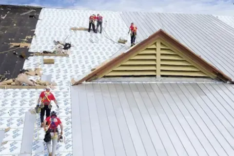 Commercial roofing crew installing metal panels on large building in Plymouth