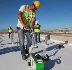 Commercial roofer operating heat welding machine on white TPO membrane seam