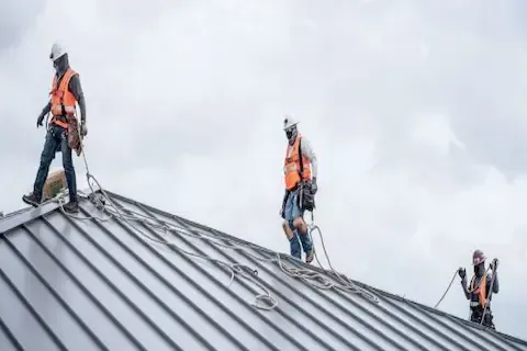 Three harnessed workers on standing seam metal roof during commercial roofing installation in Plymouth