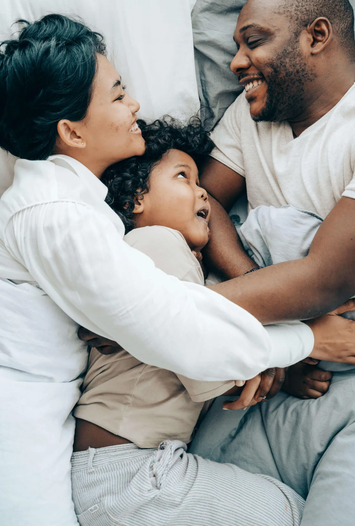 happy man and woman in bed and embracing a child lying between them