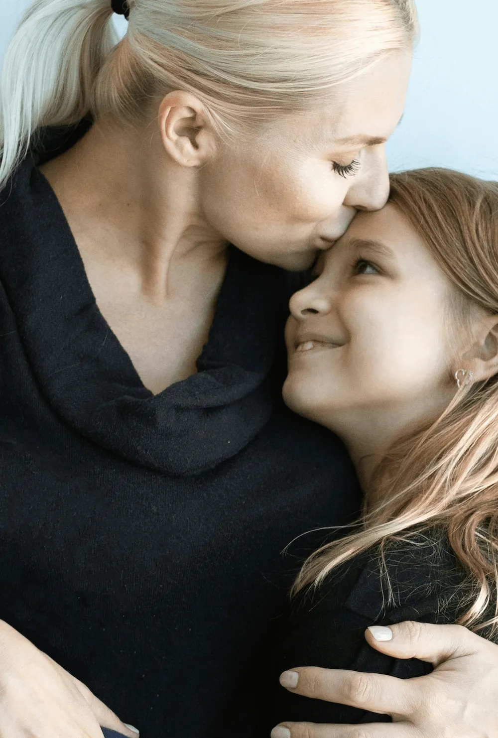 woman giving a young girl a warm embrace while kissing her on the forehead