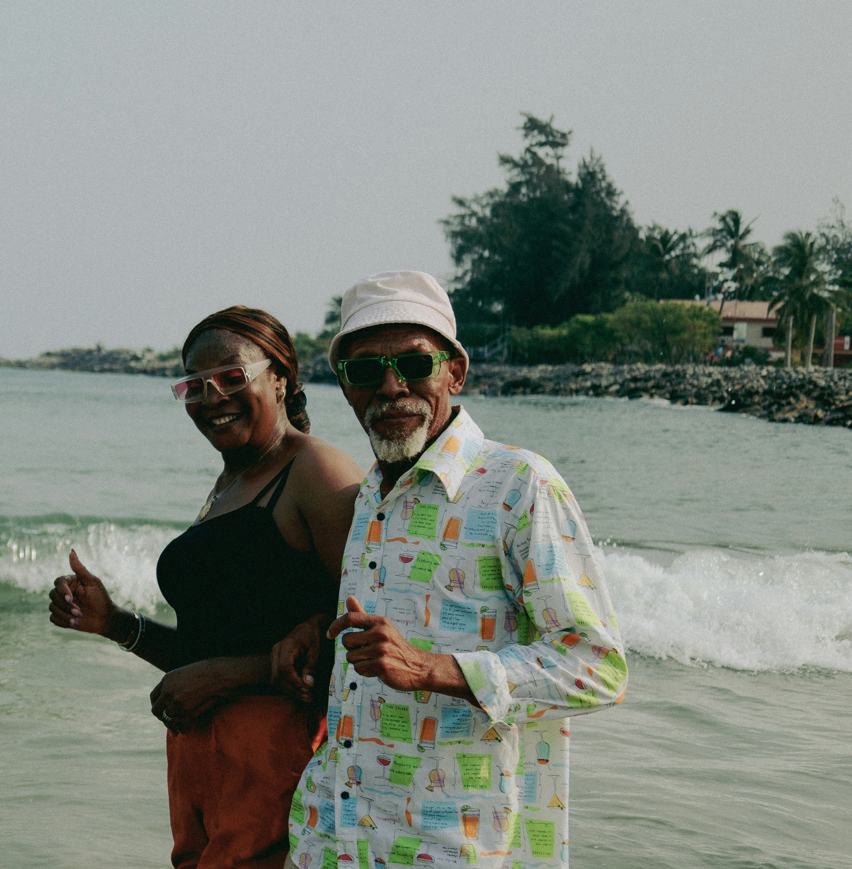 Photo of a black woman and an older man walking on the beach. In the background are palm trees and a vacation home.