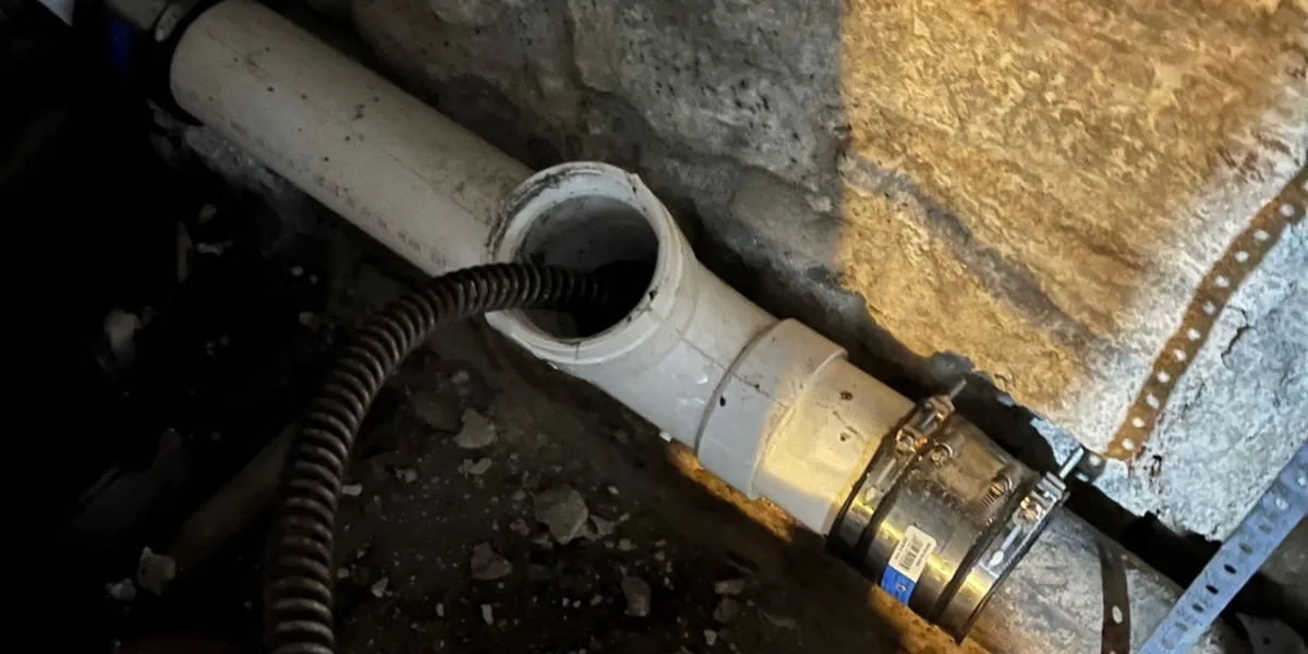 Sewer cleaning cable inserted into a PVC sewer cleanout pipe in a residential basement.