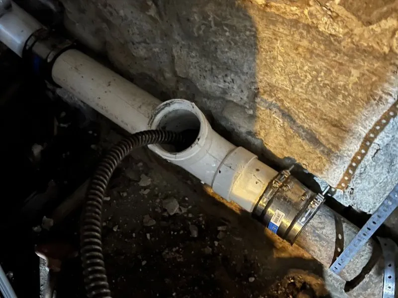 Sewer cleaning cable inserted into a PVC sewer cleanout pipe in a residential basement.