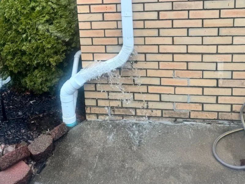 Water leaking from a downspout connection beside a brick home in Cheektowaga, NY