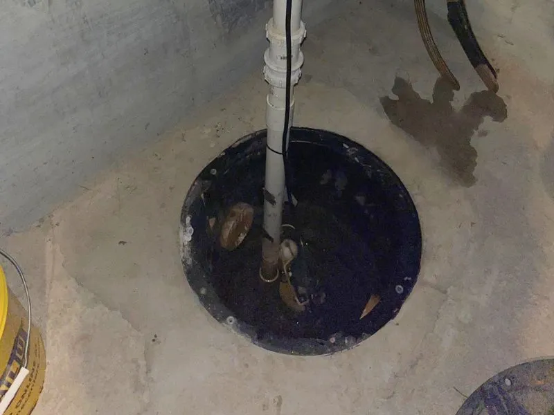 Open basement sump pit with pump and discharge piping during sump pump service