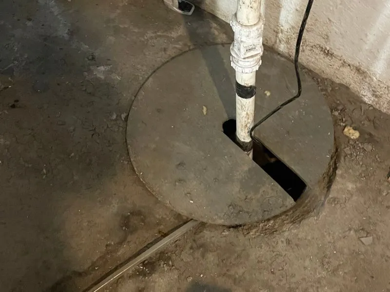 Covered basement sump pit with discharge pipe and electrical cord after sump pump service